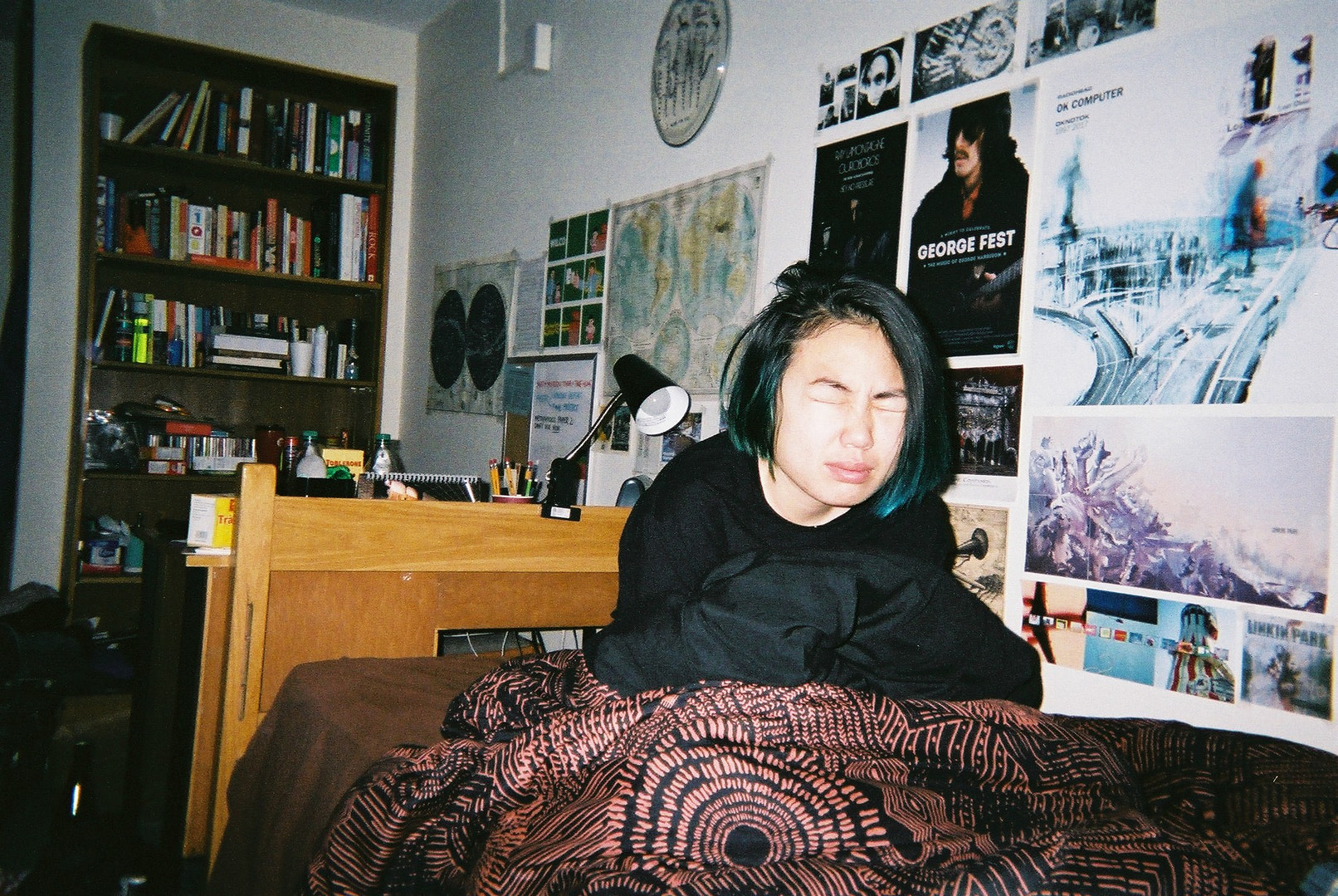 a girl in her bed looking like she just woke up, lots of posters on the wall