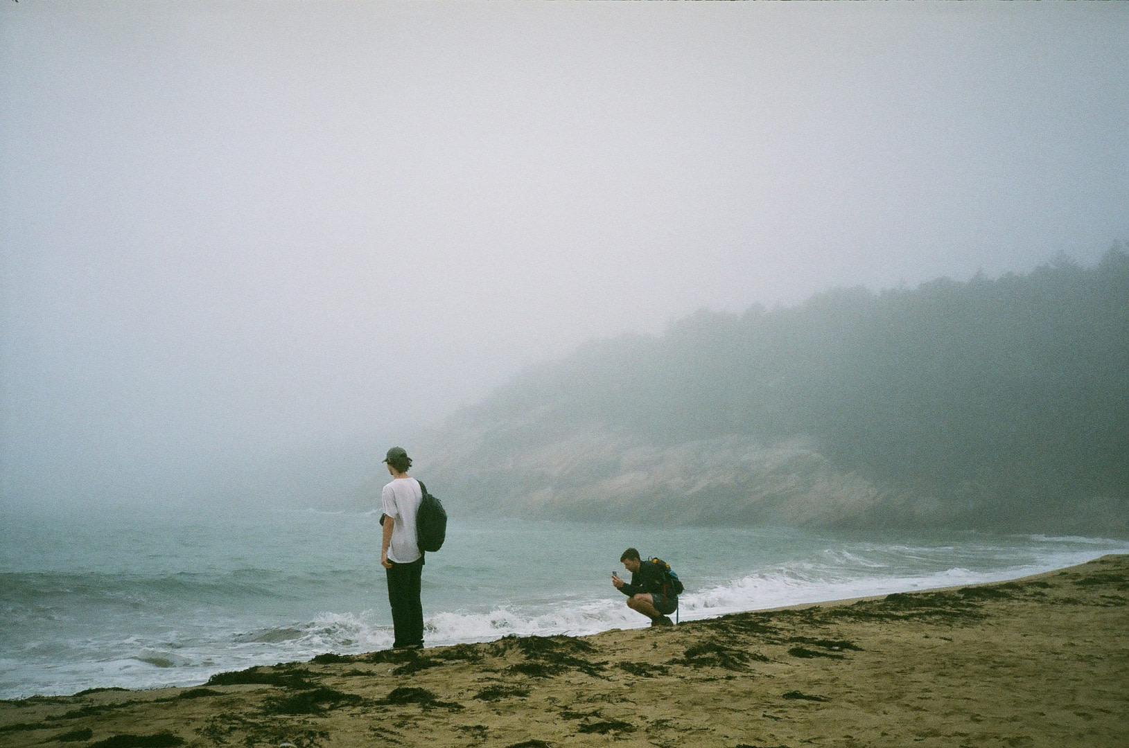 two men in the distance facing a foggy, gloomy beach