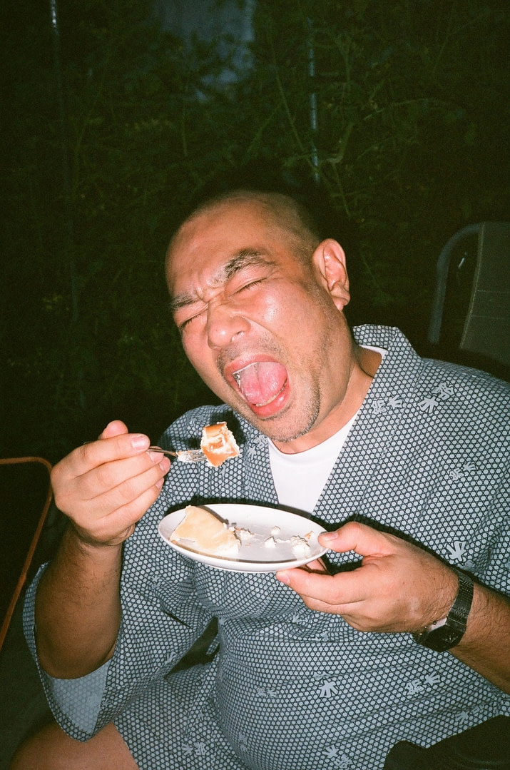 tomohiko suzuki wearing traditional japanese clothing, about to eat a cake with his mouth wide open